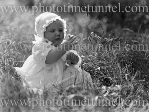 Exquisite portrait of a baby in vintage costume playing in long grass, circa 1900.